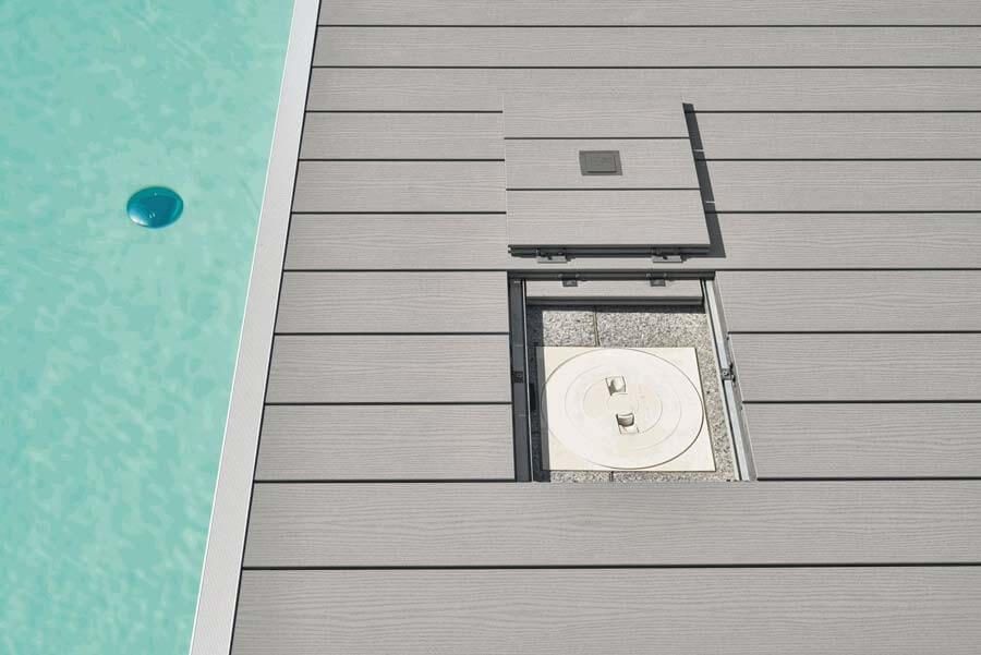 Graue Terrasse mit Revisionsschacht direkt neben einem Pool.